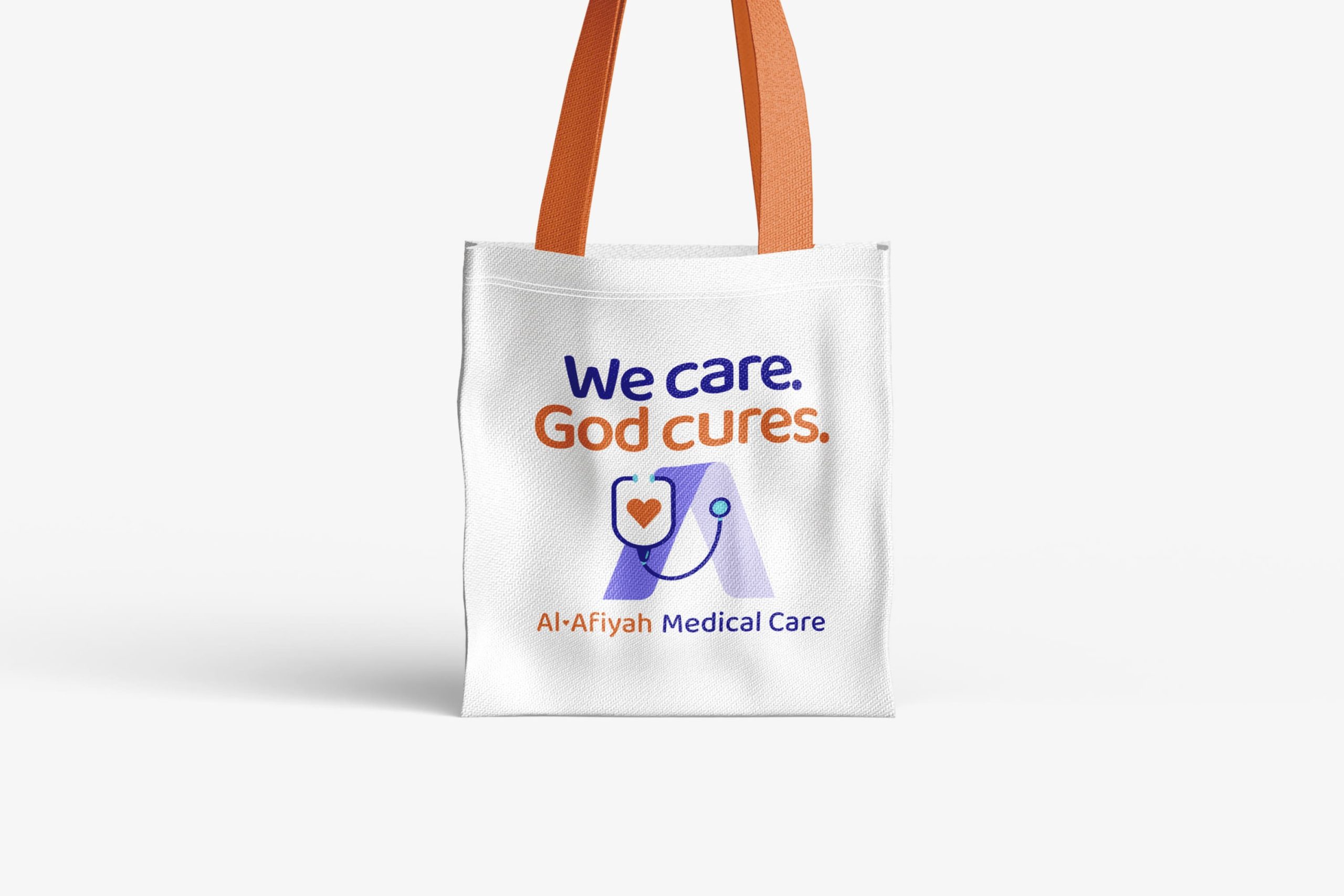 White canvas tote bag with orange shoulder straps printed with the clinic motto We care. God cures. and the Al-Afiyah Medical Care logo.