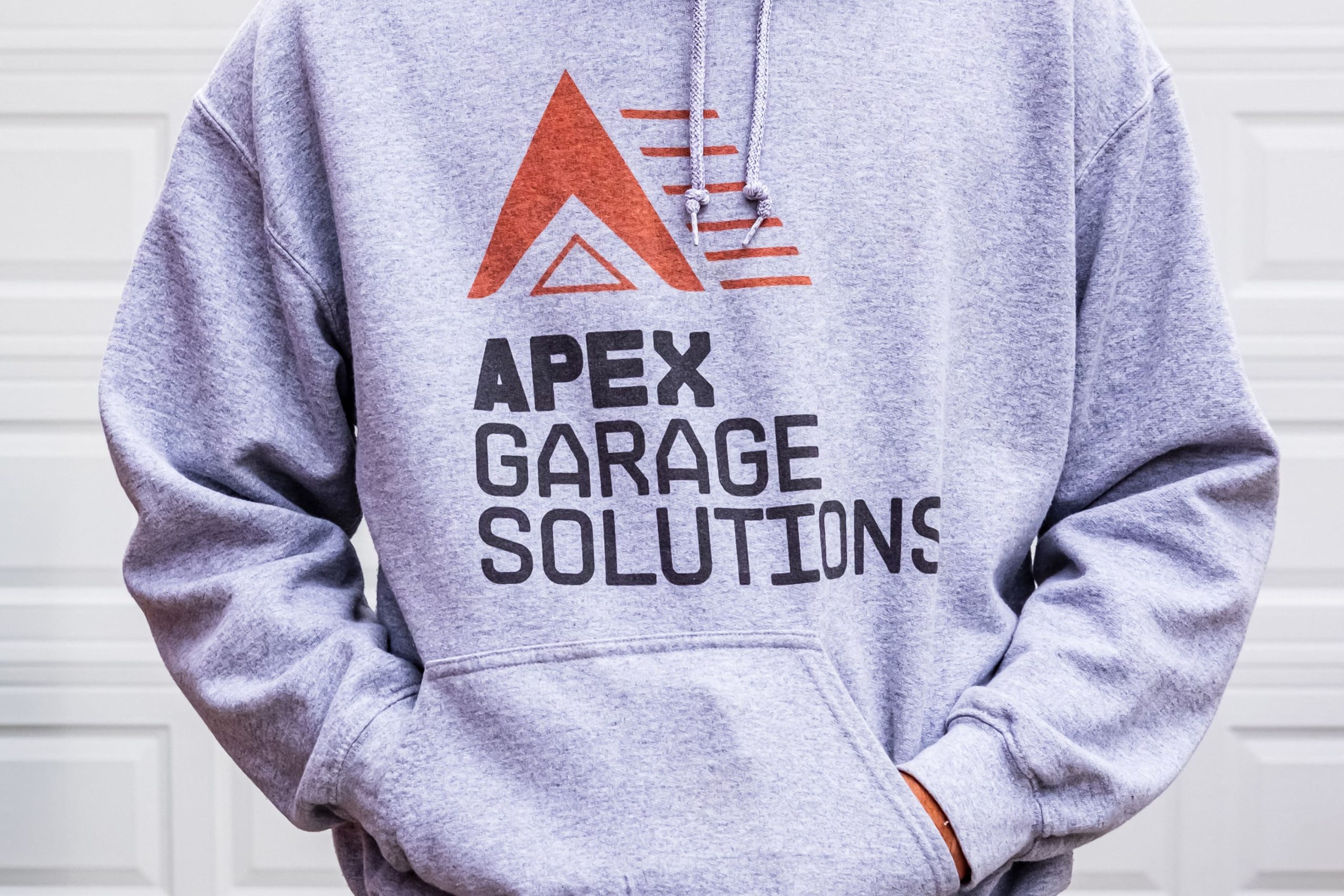 Grey pullover hoodie with the orange and black APEX Garage Solutions wordmark and chevron emblem printed across the chest.