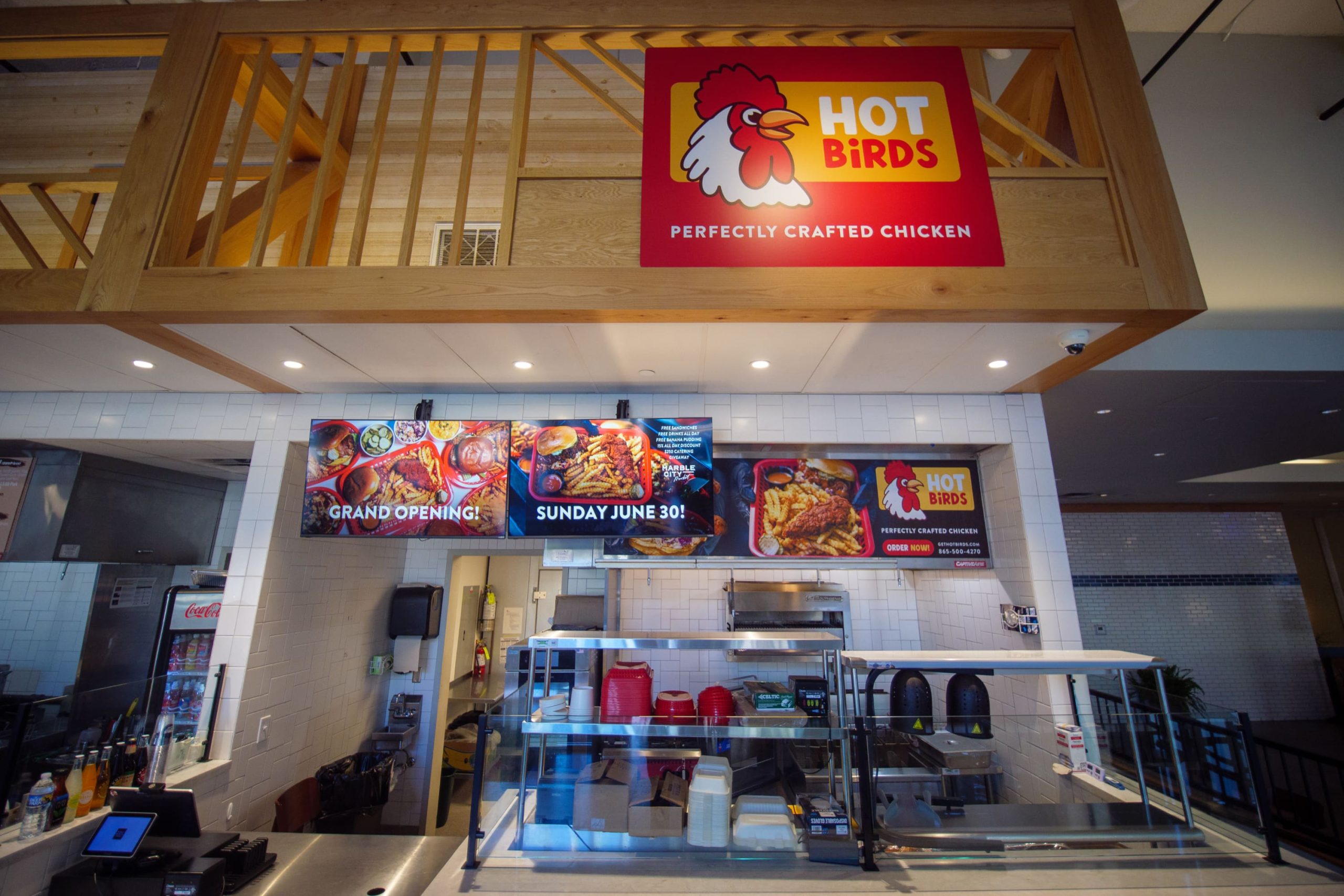 Storefront at Marble City Market with a large red overhead sign reading Hot Birds Perfectly Crafted Chicken, hanging digital menu monitors, and an order counter.